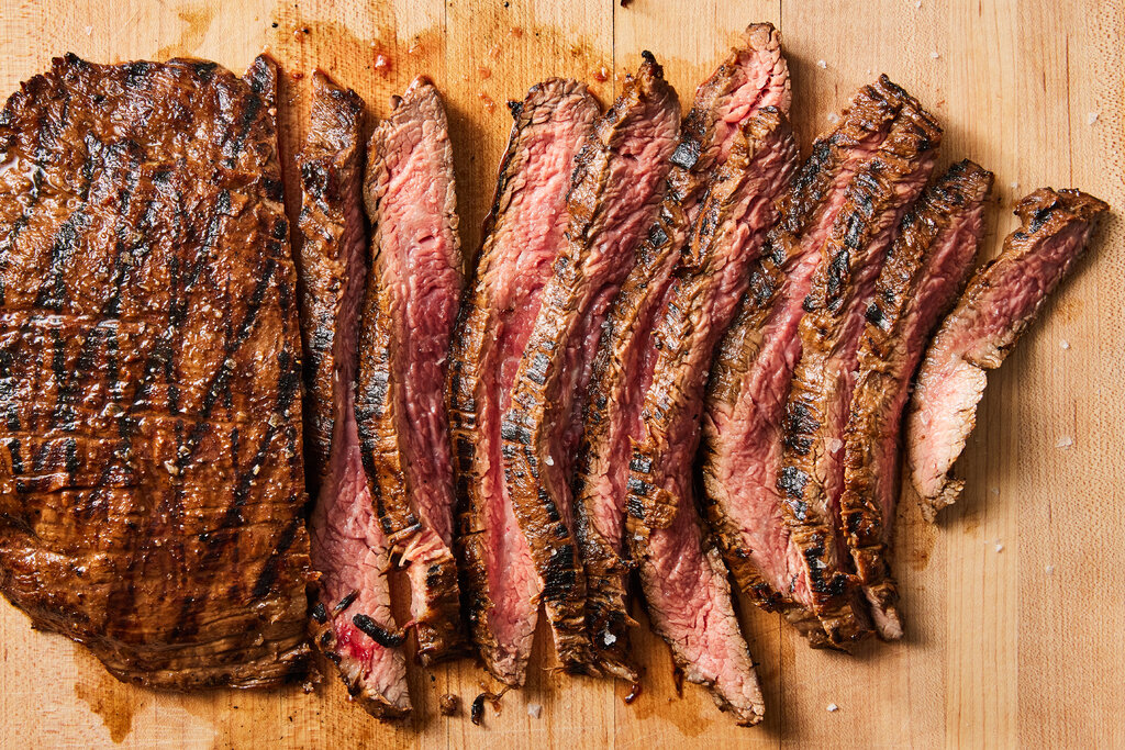 A pice of cooked steak on a cutting board, halfway cut into smaller pieces